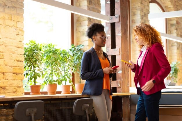 Two colleagues are having a conversation in a bright workspace. A Black woman is speaking calmly while making eye contact with a coworker who is listening attentively. The atmosphere is respectful and professional, with light streaming in from a nearby window.