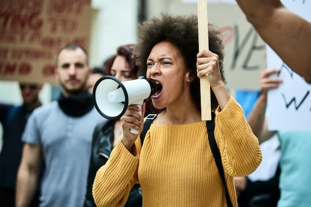A person using a megaphone at a protest, with signs advocating for policy changes and systemic reforms. The signs focus on issues such as criminal justice reform, educational equity, and affordable housing.