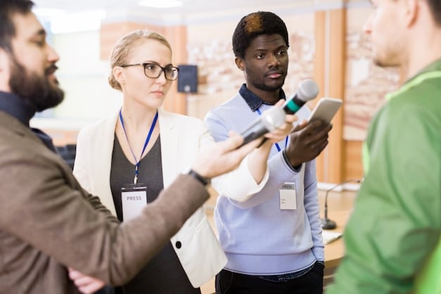 A diverse group of recruiters at a career fair booth representing a major US company. The recruiters are interacting with students from various racial and ethnic backgrounds. The booth is decorated with inclusive branding and showcasing the company's commitment to diversity and inclusion. The background shows a bustling career fair environment with many students and other company booths.